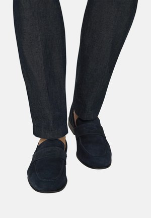 Mocassini in camoscio blu navy indossati con pantaloni di jeans blu scuro, mostrati da vista frontale e laterale su sfondo bianco.