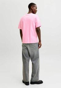 Camiseta de algodón en rosa brillante con cuello redondo, combinada con pantalones vaqueros grises holgados y zapatos negros, vista de lado y por detrás.