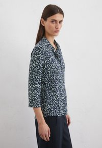 Navy und hellblau gemustertes Hemd mit kragenlosen Ausschnitt, Dreiviertelärmeln und einem lockeren Schnitt. Glatte Textur, sichtbare Knopfdetails.