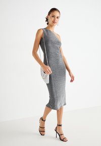 Rochie gri, cu un singur umăr, într-un design ajustat, cu o textură strălucitoare. Asortată cu sandale negre cu bretele și o geantă de umăr cu mărgele argintii.