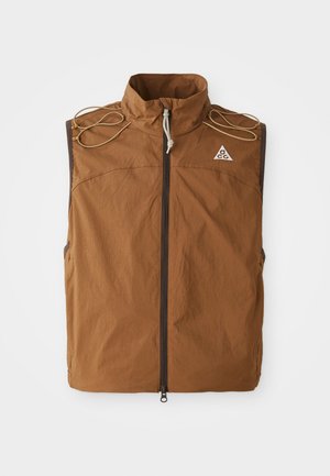Brun vest med høy krage, frontglidelås og skulderbånd. Laget av lett stoff, med en logo på øvre venstre side.