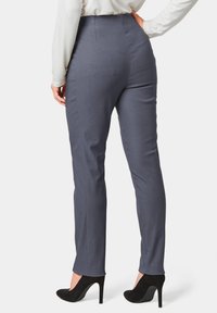 Graue maßgeschneiderte Hose mit hoher Taille und glatter Textur. Figurbetonte Silhouette, die an den Knöcheln endet, kombiniert mit schwarzen high heels.
