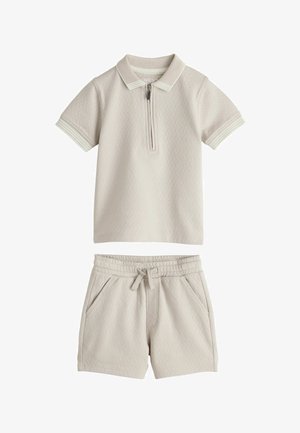 Svetlobéžové polo tričko s krátkym rukávom a štvrťovým zipsom, textúrovaná tkanina a pruhovaný golier; krátke nohavice v rovnakej farbe s elastickým pásom a bočnými vreckami.