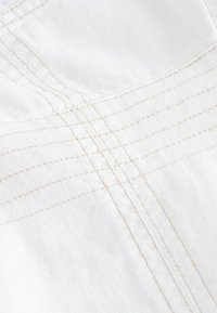Gros plan d'un tissu blanc avec des points de fil beige entrecroisés formant un motif en croisillons sur une surface texturée.