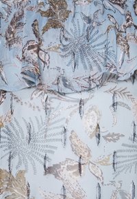 Tissu bleu clair avec des motifs floraux et de fougères aux tons chauds, agrémenté d'accents en sequins argentés et d'un bord froncé. Texture lisse.