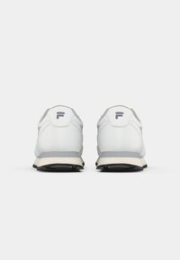 White athletic shoes with a smooth synthetic upper, grey accents, a reinforced heel, and a textured black rubber sole. Logo displayed at the back.