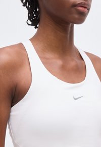 Κοντινό πλάνο ενός ατόμου που φοράει λευκό αθλητικό τοπ της Nike, δείχνοντας τους ώμους, τον λαιμό και μερικά από το πρόσωπο, σε απλό φόντο.