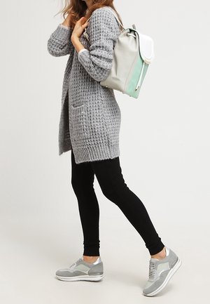 Cardigan lavorato a maglia grigio chiaro con tasche, leggings neri e sneakers grigie con dettagli argento. Zaino in grigio chiaro e verde menta.