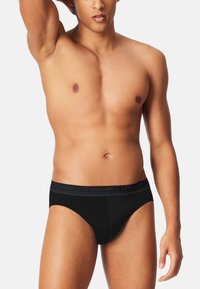 Sorte kort underbukser med struktureret stof og en blød linning med mærket "UNCOVER" i et subtilt mønster. Glat, tætsiddende design.