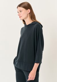Felpa nera con una vestibilità comoda, dotata di cappuccio, maniche a tre quarti e una texture liscia. Abbinata a pantaloni scuri coordinati.