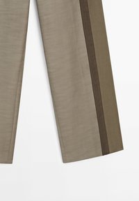Pantalon beige à texture lisse, avec des bandes latérales marron foncé. Coupe droite, fabriqué en tissu léger.