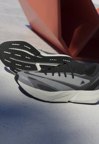 Atletske cipele s gornjim dijelom u crnoj i sivoj boji, s teksturiranim dizajnom i bijelim LIGHTSTRIKE međupodiškom. Guma potplat s utorima za prianjanje.