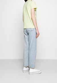 Camiseta de manga corta verde claro combinada con jeans de corte holgado azul claro y zapatillas blancas. Diseño sencillo sin patrones ni acentos visibles.