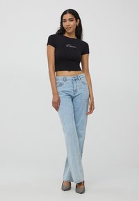 Czarna krótka bluzka z krótkimi rękawami i haftem "Rêverie", w połączeniu z jasnoniebieskimi spodniami o wysokim stanie i błyszczącymi czarnymi szpilkami.