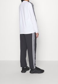 White long-sleeve shirt with black side stripes, paired with gray pants featuring white stripes. Black athletic shoes complete the look.