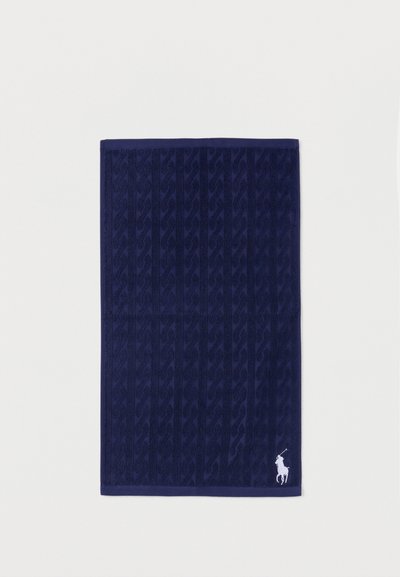 Σκούρα μπλε πετσέτα με διακριτικό ριγέ υφή και λευκό κεντημένο λογότυπο παίκτη πόλο στην κάτω δεξιά γωνία.