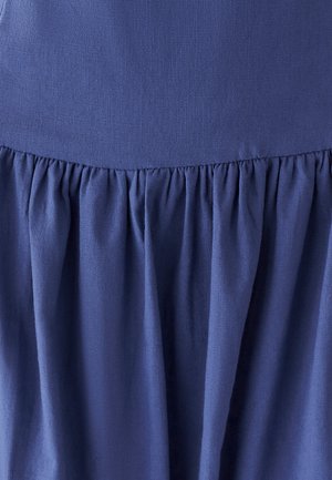 Tissu bleu avec une texture lisse, présentant un détail de jupe froncée en bas. Le matériau semble léger et tombe doucement.