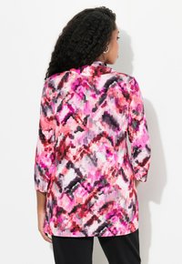 Helle, farbenfrohe Bluse mit einem pinken und schwarzen abstrakten Muster, aus leichtem Material gefertigt, mit Dreiviertelärmeln und einem Kragen.