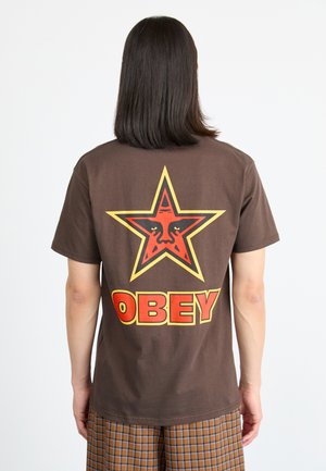 Brown cotton T-shirt featuring a large red and yellow star graphic with a face, and the word "OBEY" in bold red letters below.