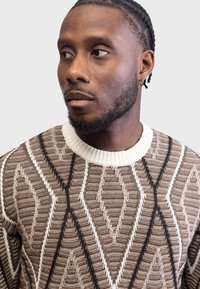 Knit sweater in brown and beige with a diamond pattern. Features a cream ribbed collar and dark accents throughout the design.