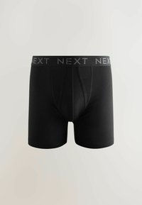Crne bokserice od mekog materijala, s širokim elastičnim pojasom na kojem je logo "NEXT". Dizajn uključuje tradicionalni otvor.