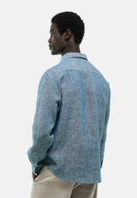 Chemise en lin bleu clair avec une coupe décontractée, manches longues et col classique. Texture subtile et tissu léger pour une respirabilité optimale.