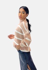 Hellrosa Strickpullover mit weißen Streifen, Funnel-Neck und überschnittenen Schultern. Kombiniert mit einem dunklen Jeansrock mit seitlichem Schlitz.