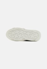 Fehér sneaker talp, csillag alakú taposó mintázattal, gumiból készült, textúrált felülettel és sima szélekkel a tapadás érdekében.