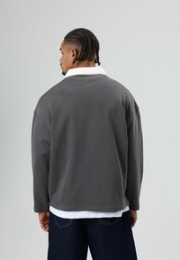 Oversized grijze trui met een witte kraag, zachte textuur en lange mouwen. Gecombineerd met een donkerblauwe spijkerbroek. Achteraanzicht.