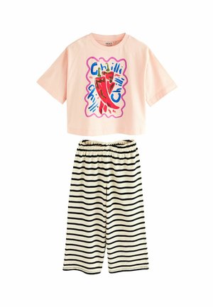 Avskuren rosa t-shirt med färggrafisk chilipeppar; ihopparad med svart-vita randiga lösa shorts med elastisk midja.