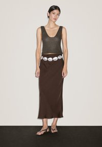 Jupe maxi marron avec une texture lisse, accompagnée d'un top en tank court en maille côtelée de couleur marron foncé. Un détail de ceinture circulaire en argent met en valeur la taille.