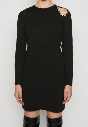 Czarna sukienka z długim rękawem z wycięciem na ramieniu ozdobionym perłowymi akcentami, wykonana z gładkiej tkaniny o dopasowanym kroju.