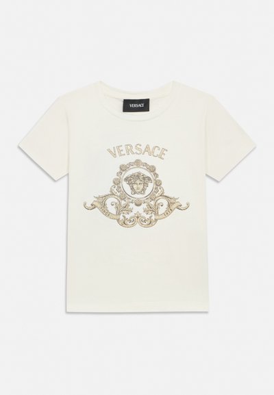 Λευκό κοντομάνικο μπλουζάκι με χρυσό διακοσμητικό έμβλημα Μέδουσας και το κείμενο "VERSACE" από πάνω στο μπροστινό μέρος, στρογγυλή λαιμόκοψη και μαύρη ετικέτα λογότυπου στη εσωτερική πλευρά του γιακά.