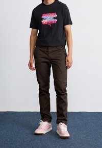 T-shirt nera a maniche corte con stampa grafica, pantaloni marroni svasati e sneakers rosa. Tessuto morbido con colori a contrasto e dettagli di design.