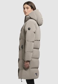 Garš beidžs pūšamais mētelis ar kapuci, ar rāvējslēdzēju priekšpusē, sānu kabatām un teksturētām daļām. Iekļauj logotipa plāksni netālu no pleca.