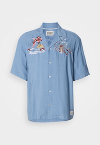 Ανοιχτό μπλε κοντομάνικο πουκάμισο με κλείσιμο με κουμπί και κεντημένα σχέδια μιας rose, ήλιου, κυμάτων και ενός κτιρίου στη αριστερή πλευρά.