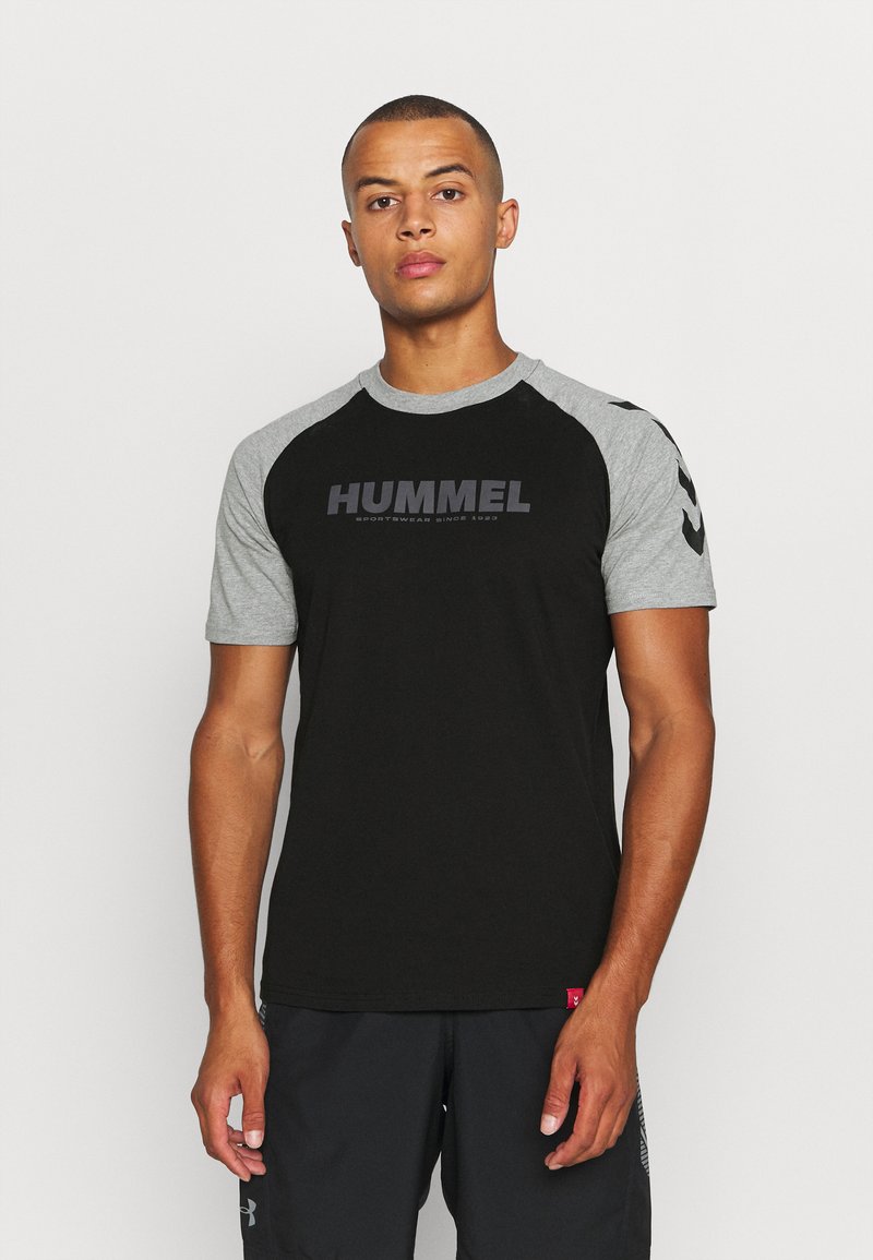 Svart T-skjorte med korte ermer og grå raglaner, med "HUMMEL" logo trykket i en mørk nyanse på forsiden.