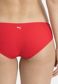 Rote Badeunterteile aus glattem Stoff. Mit einem tiefen Schnitt und einem weißen Puma-Logo auf der Rückseite. Sauberes Design, keine zusätzlichen Muster.