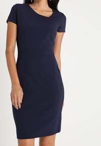 Mörkblå klänning i stretchigt material, med rund halsringning, korta ärmar och en figurnära siluett som når knäna.