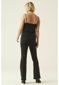 Camisole noire avec dentelle associée à un jean évasé taille haute noir. Le mannequin porte des chaussures à talons noires, vue de dos avec peu de détails.