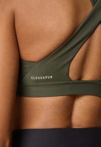 Sujetador deportivo verde oliva con la espalda baja, con tirantes entrecruzados y la palabra "CLOUDSPUN" en letras claras cerca de la banda.