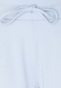 Bela platnena hlače z zavezanim pasom z vrvico, prikazani so podroben tekstura in šivi na enobarvnem ozadju.