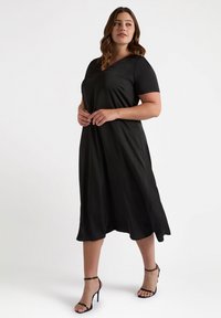 Vestido negro midi con escote en V y mangas cortas. Tejido suave y ligero que cae suavemente más allá de las rodillas. Combinado con tacones negros con tiras.