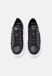 Svarte joggesko med glatt skinn på tåhetten, teksturerte svarte sidestykker, sølvfarget metallbeslag og hvit gummisåle. Snørredesign og logodetalj.