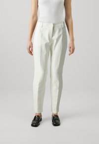 White tailored pants with a smooth texture, slim fit, and slight tapering at the ankles. Worn with black loafers.
