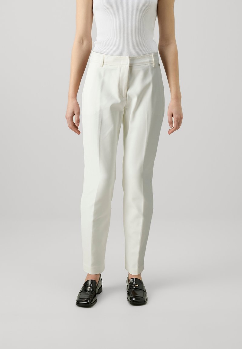 White tailored pants with a smooth texture, slim fit, and slight tapering at the ankles. Worn with black loafers.