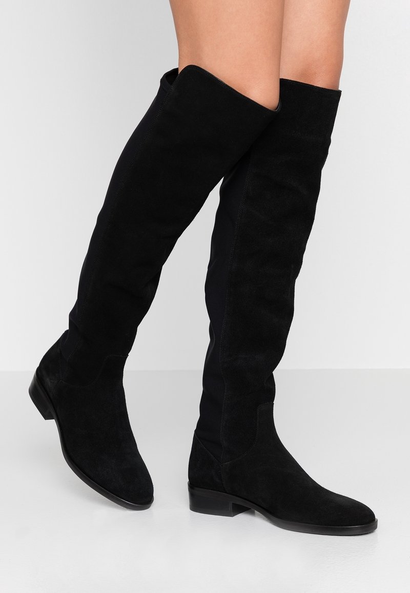 Botas de ante negras por encima de la rodilla con un diseño ajustado, punta redonda y tacón plano. La parte superior incluye paneles laterales elásticos para mayor comodidad.