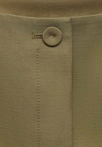 Tkanina khaki o gładkiej fakturze, z zapięciem na guziki i starannym przeszyciem wzdłuż szwu bocznego. Prosty i funkcjonalny design.