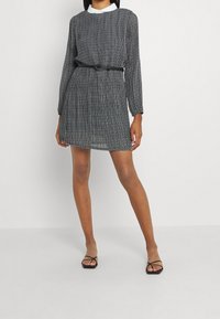 Svart och vit randig långärmad klänning med midjebälte, veckad design och vit krage. Bärs med svarta sandaletter med remmar.