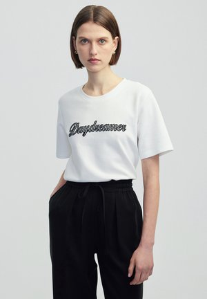 White short-sleeve T-shirt featuring black embroidered text "Daydreamer." Paired with black high-waisted trousers with a drawstring waist.